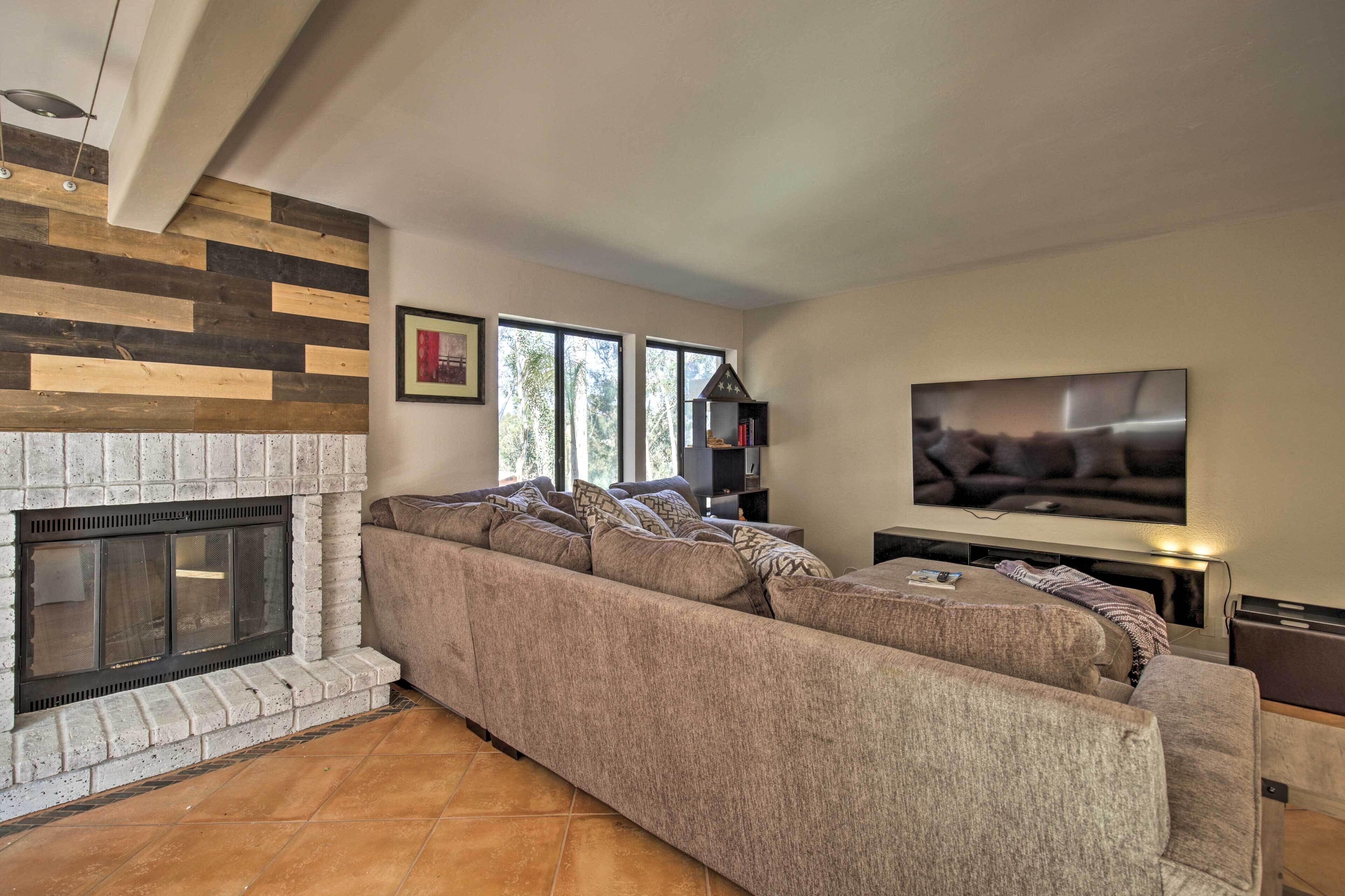 A living room with a sectional sofa, a fireplace, a flat-screen TV, and large windows.