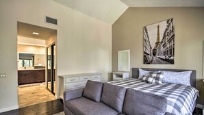 Un dormitorio con una cama grande, un sofá gris, un cuadro de la Torre Eiffel y vistas a la cocina.