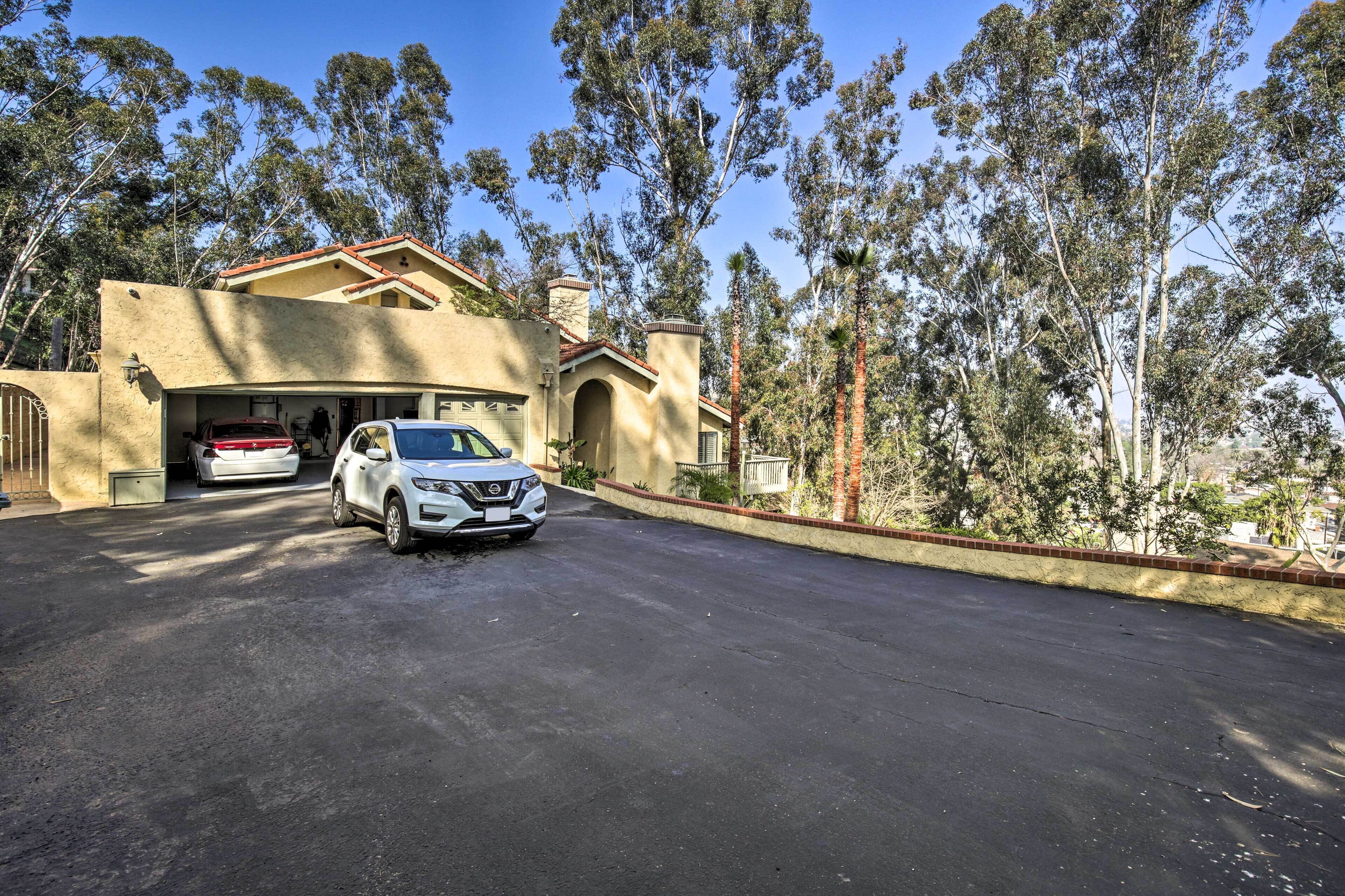 Uma casa de dois andares com garagem, carros estacionados e uma entrada com acesso por um caminho.