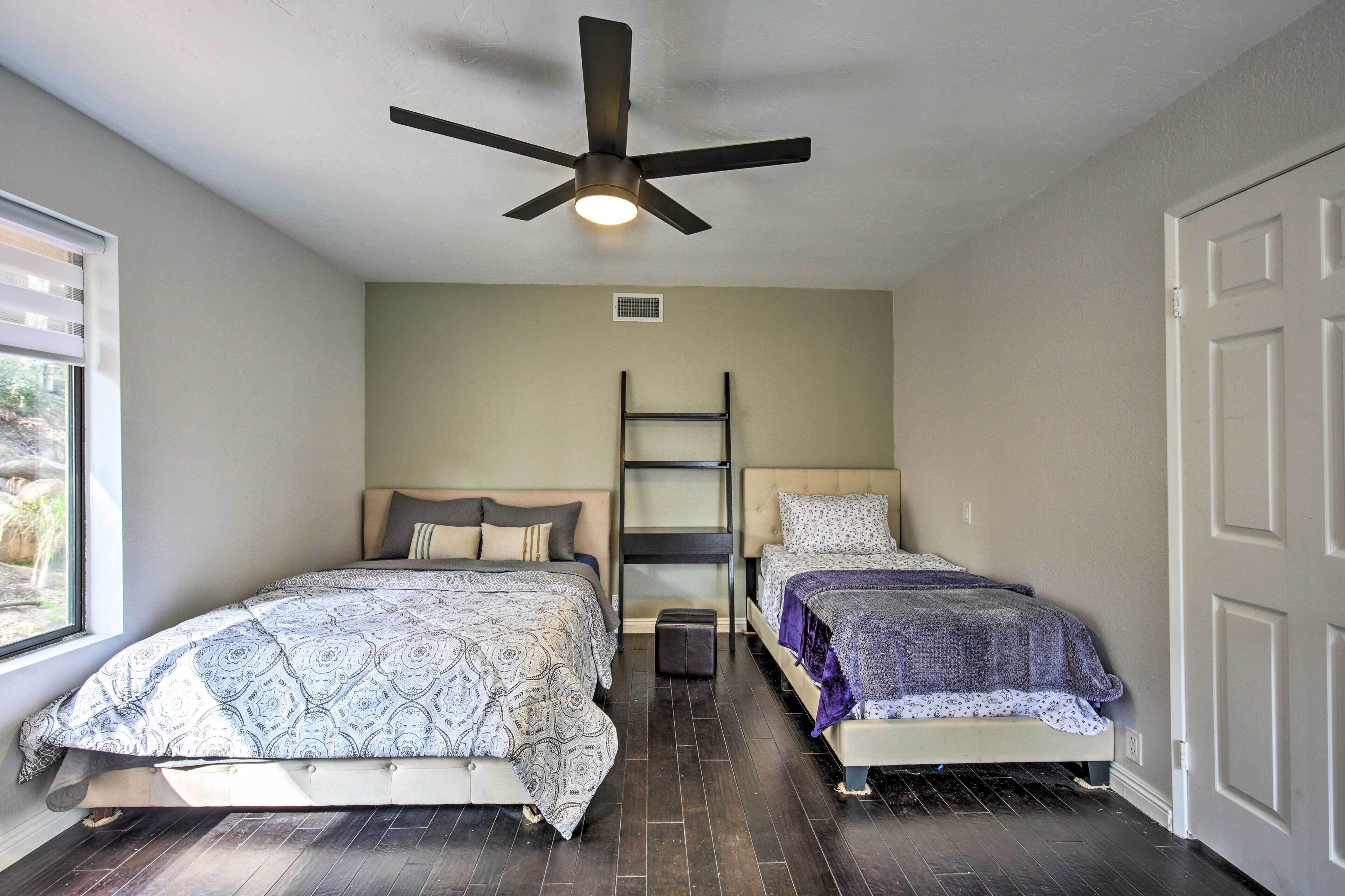 A bedroom with two beds, a ceiling fan, a window, and a door.