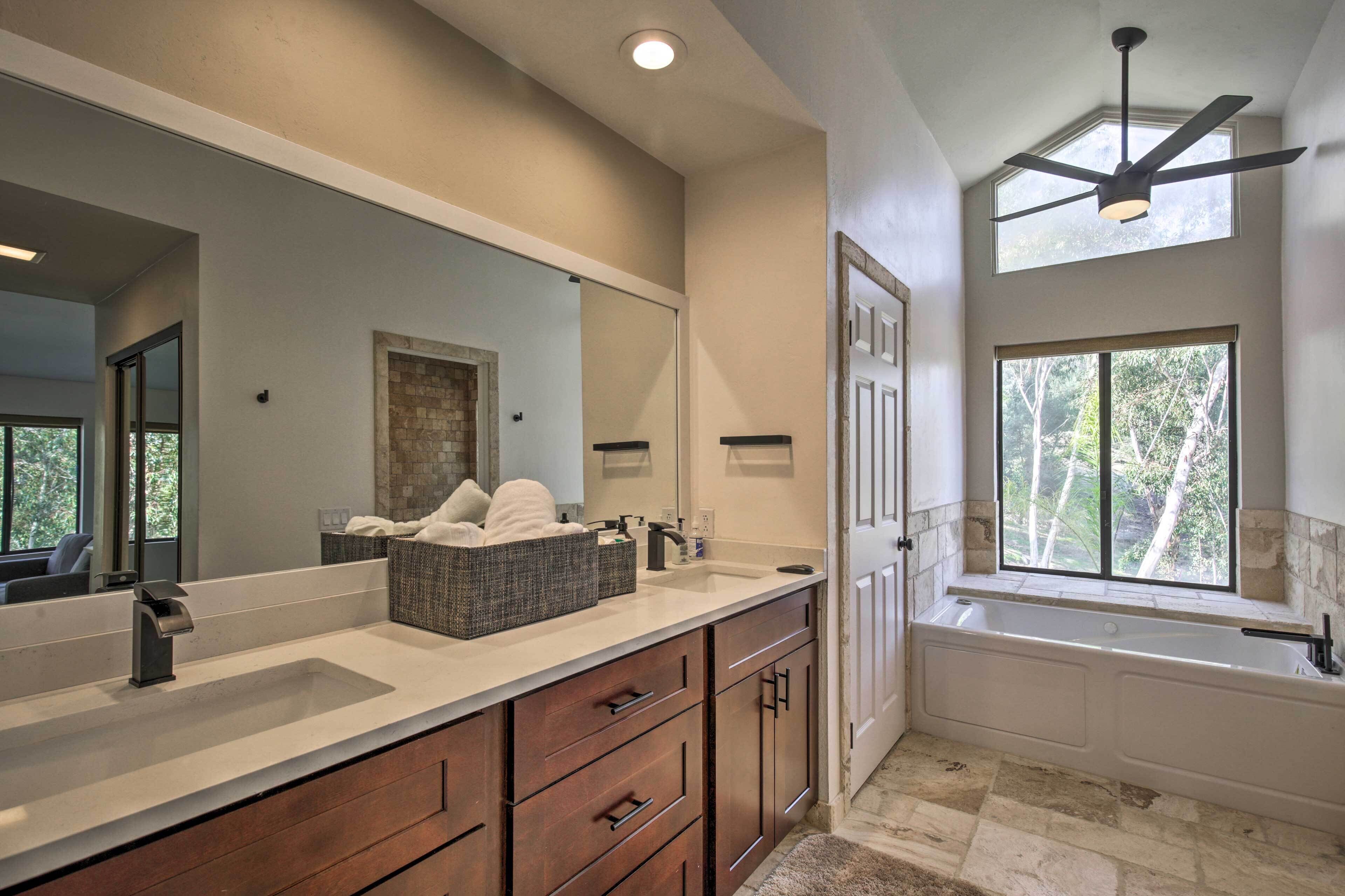 Une salle de bain moderne avec un grand miroir, deux lavabos, une baignoire et un ventilateur de plafond.