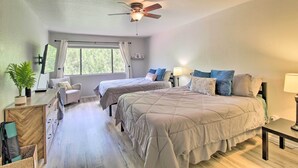 Een slaapkamer met twee bedden, een plafondventilator, een raam met gordijnen, een bureau met stoel en een potplant.