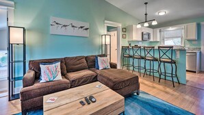 A modern living room with a sectional sofa, a coffee table, and a kitchen area with bar stools.