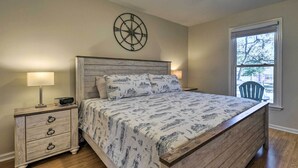 A bedroom with a wooden bed, a nightstand with drawers, a compass wall decoration, and a window with a view of the outside.