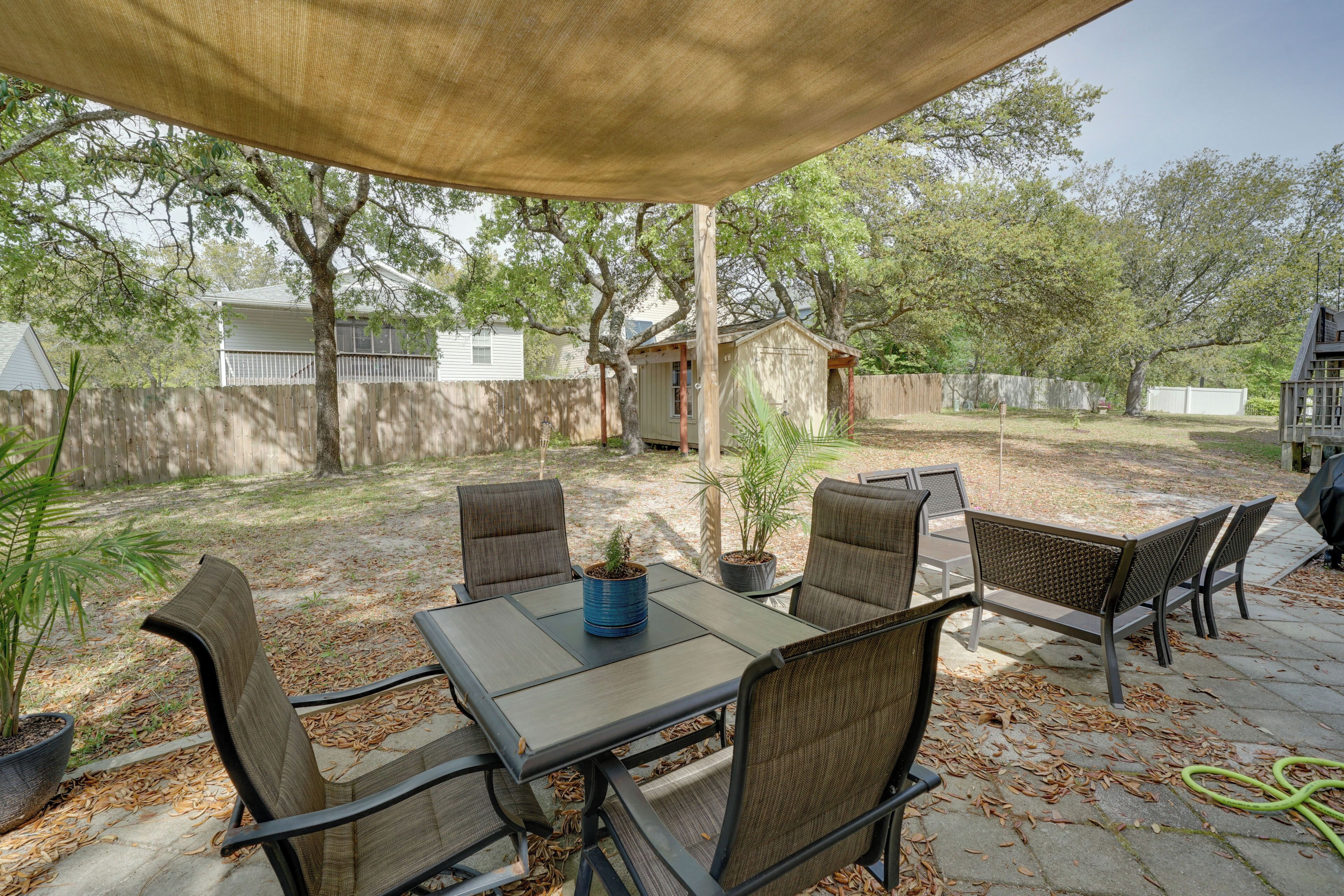 An outdoor patio with a table and chairs, surrounded by trees and a covered area.