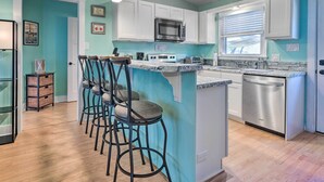 A kitchen with a teal accent wall, white cabinets, a stainless steel dishwasher, and a bar area with stools.