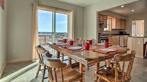 A spacious dining area with a long table set for six, wooden chairs, and a view through large windows. - Rural Base Camp for Grand Canyon, Zion & Bryce NP! (Kanab)