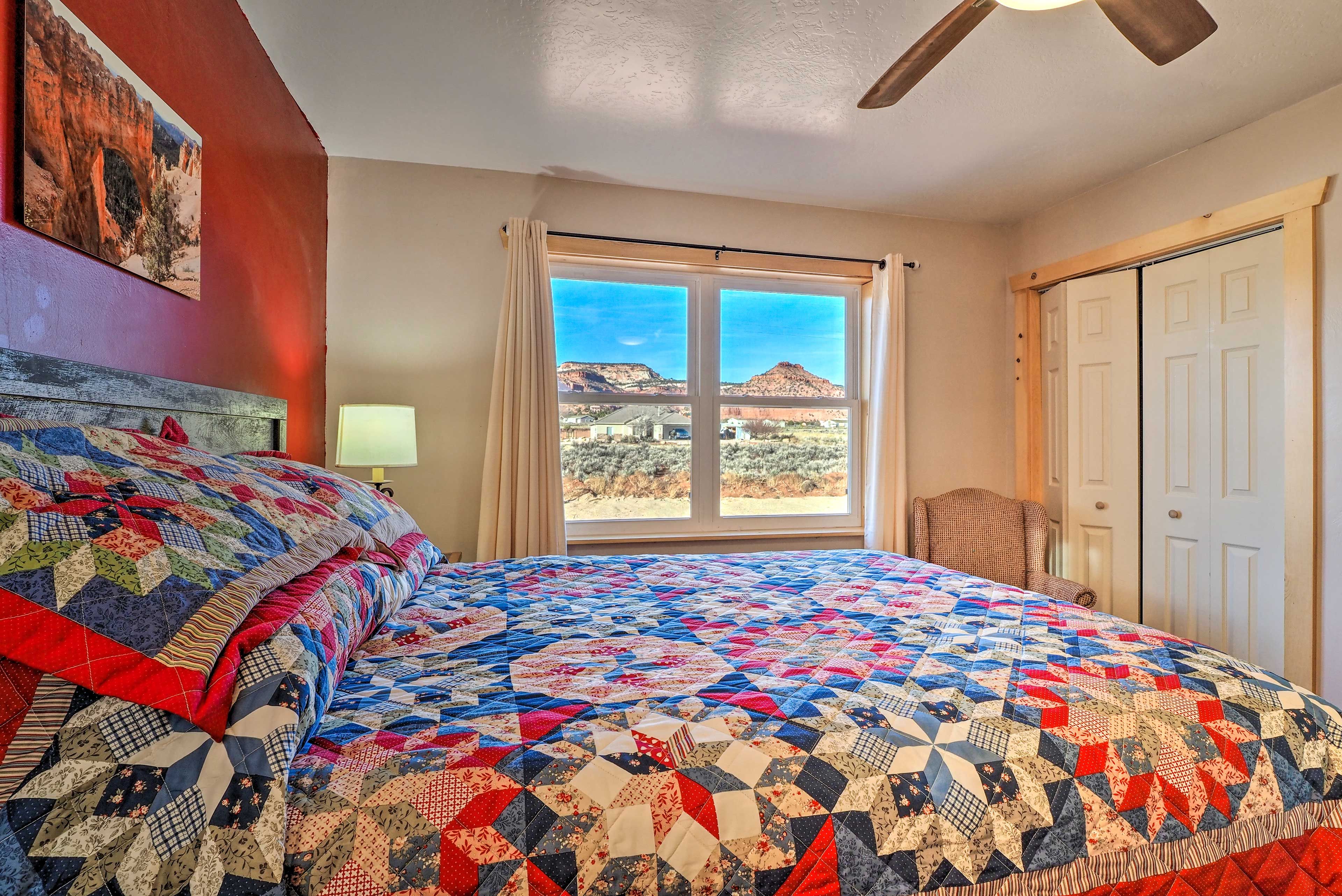 Une chambre avec un grand lit, une fenêtre donnant sur une montagne, un ventilateur de plafond et une porte.
