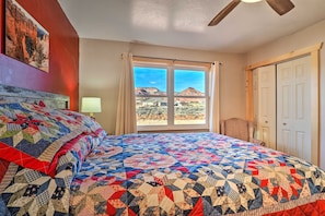 A bedroom with a large bed, a window with a view of a mountain, a ceiling fan, and a door.