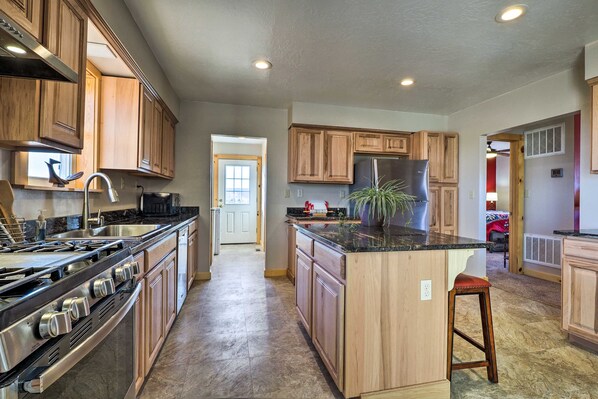 A spacious kitchen with wooden cabinets, a central island, stainless steel appliances, and a view into the living area.