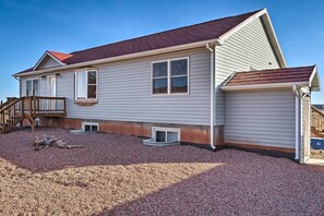 A two-story house with a red roof, a wooden deck, and a gravel driveway.