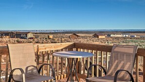A wooden deck with two chairs and a table, overlooking a desert landscape with houses in the distance. - Rural Base Camp for Grand Canyon, Zion & Bryce NP! (Kanab)