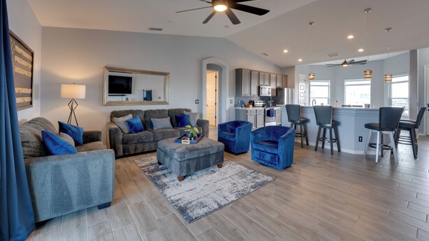 A spacious living area with a ceiling fan, a kitchen in the background, and a bar area with high stools. - Pool & Patio: Newly Constructed Lake Havasu Home! (Lake Havasu City)