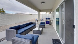 A covered patio area with a seating arrangement, a table, and a grill. - Pool & Patio: Newly Constructed Lake Havasu Home! (Lake Havasu City)