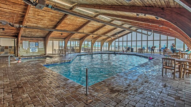 An indoor swimming pool with a wooden ceiling and brick flooring, surrounded by seating areas. - Steps to Shore: Beachfront Studio w/ Pool Access! (Myrtle Beach)