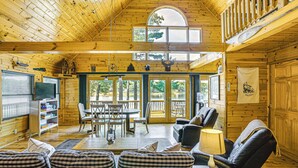 A wooden cabin interior with a dining area, seating, and a television. - Peaceful Long Lake Cottage w/ Deck, Dock & Kayaks! (Branch)