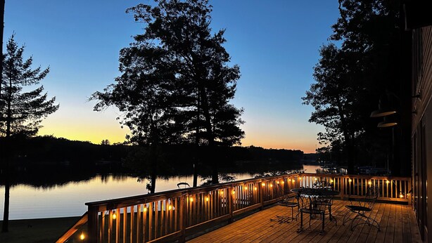 A wooden deck with a railing, overlooking a calm lake at dusk. - Peaceful Long Lake Cottage w/ Deck, Dock & Kayaks! (Branch)