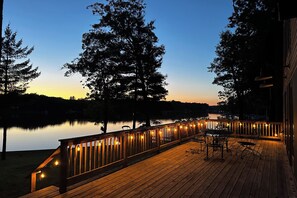 A wooden deck with a railing, overlooking a calm lake at dusk. - Peaceful Long Lake Cottage w/ Deck, Dock & Kayaks! (Branch)