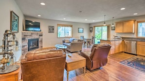 A spacious living area with a fireplace, leather seating, a flat-screen TV, and a kitchen with wooden cabinets and a dishwasher. - Hammond Home 2 Blocks to Marina & Columbia River! (Hammond)