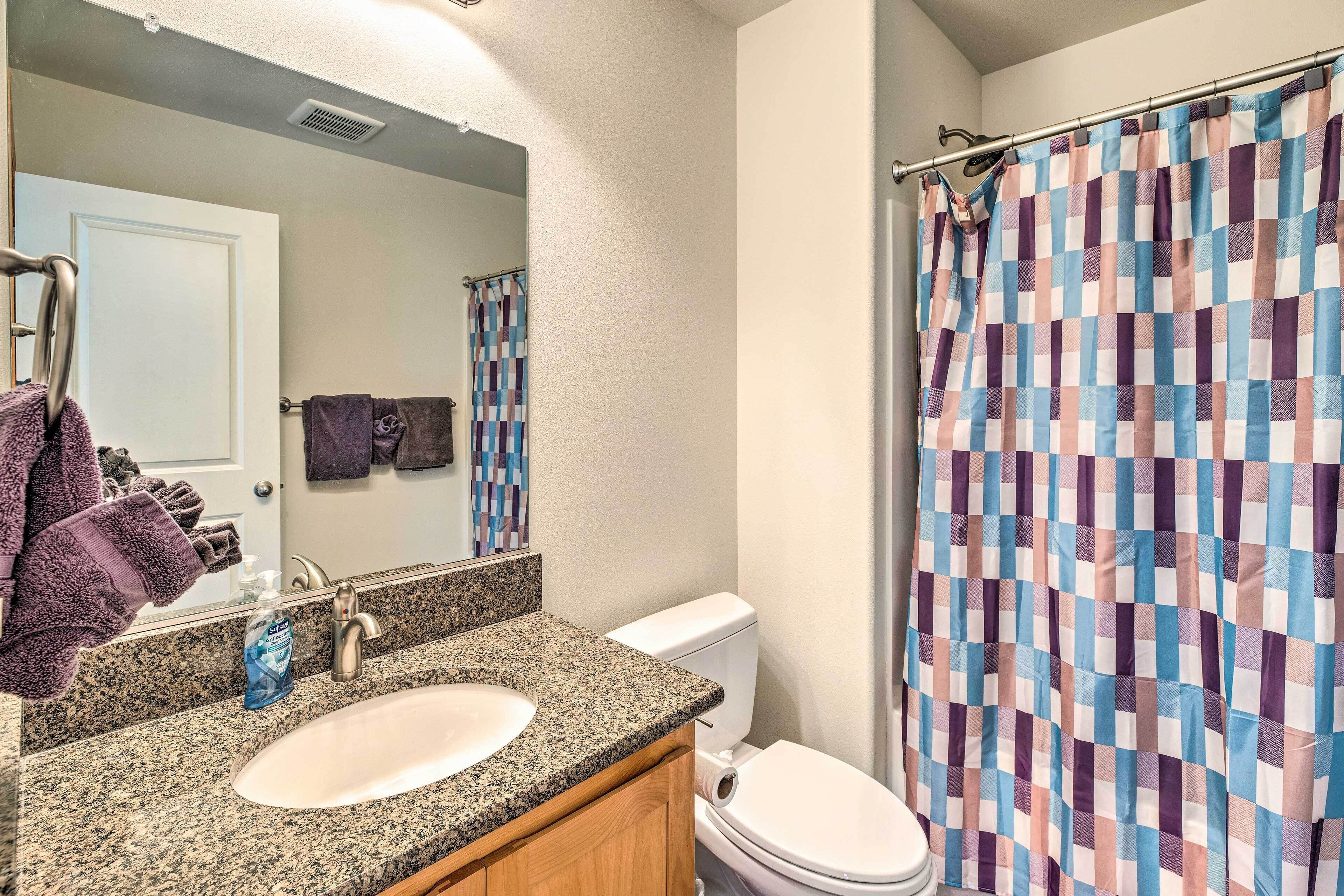 A bathroom with a granite countertop sink, a mirror, a white toilet, and a checkered shower curtain.