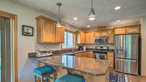 A kitchen with granite countertops, wooden cabinets, stainless steel appliances, and blue bar stools.