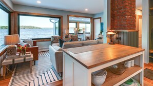 A modern living room with a large window, a fireplace, and a dining area with a wooden table. - Winnipesaukee Lakefront Home With Dock & Views! (Alton Bay)