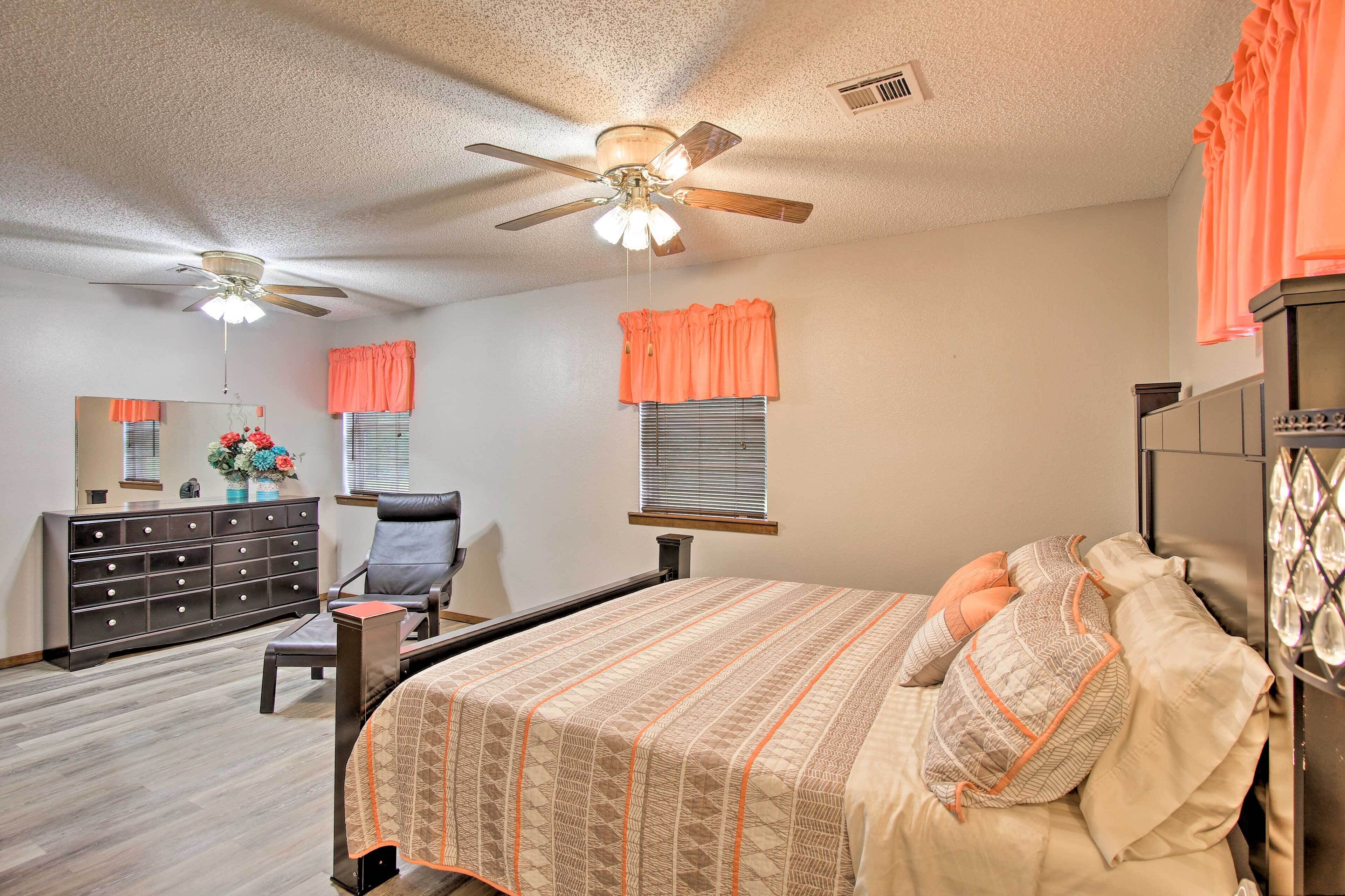 A bedroom with a bed, a dresser, a chair, a ceiling fan, and a window with blinds.