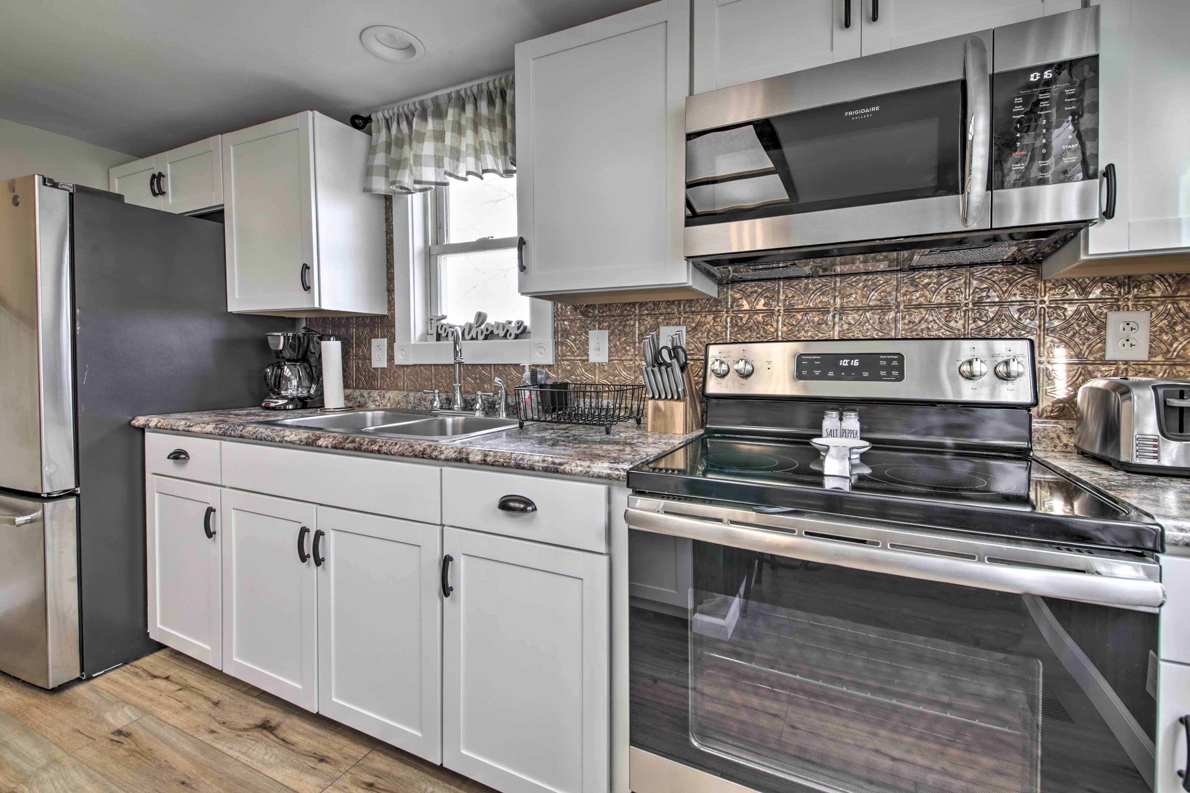 Een moderne keuken met witte kasten, roestvrijstalen apparatuur, een granieten aanrechtblad en een decoratieve achterwand.