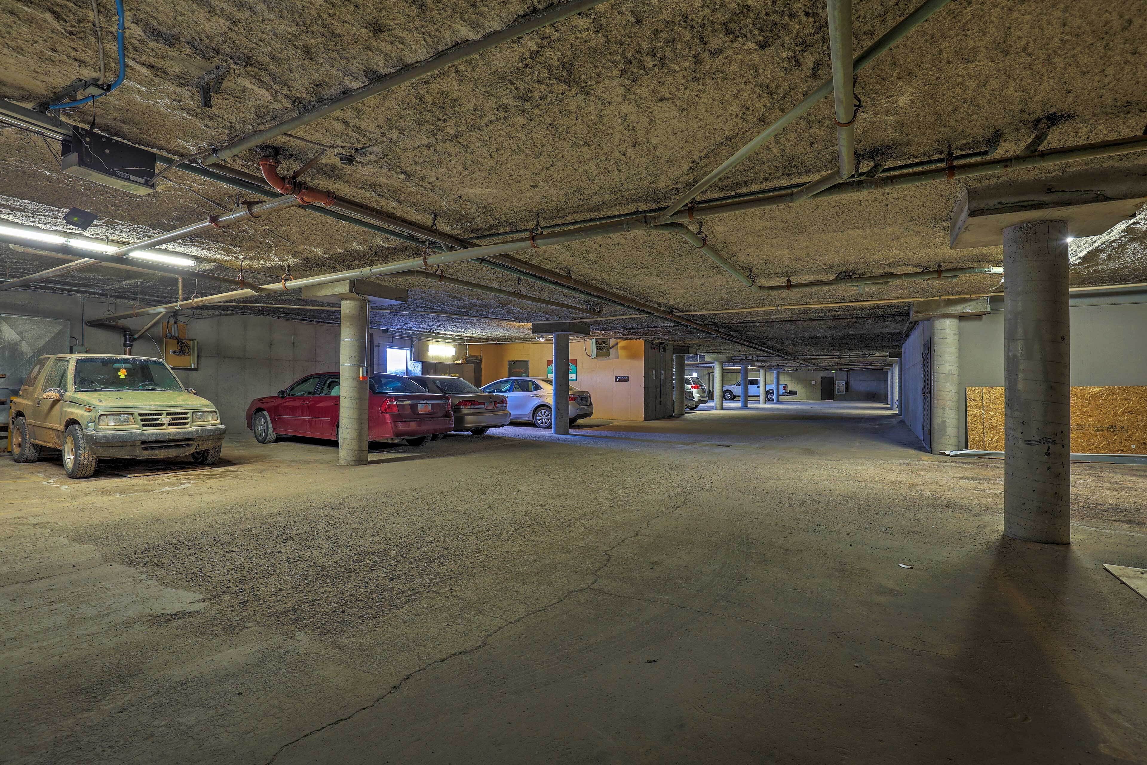 Un parking souterrain avec des piliers en béton, un éclairage fluorescent et plusieurs voitures garées.