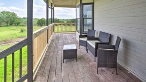 Eine überdachte Veranda mit Korbmöbeln, einem kleinen Tisch und Blick auf ein grasbewachsenes Feld.