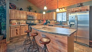 Une cuisine avec des meubles en bois, un réfrigérateur en acier inoxydable, un grand îlot central avec des tabourets et des luminaires suspendus.