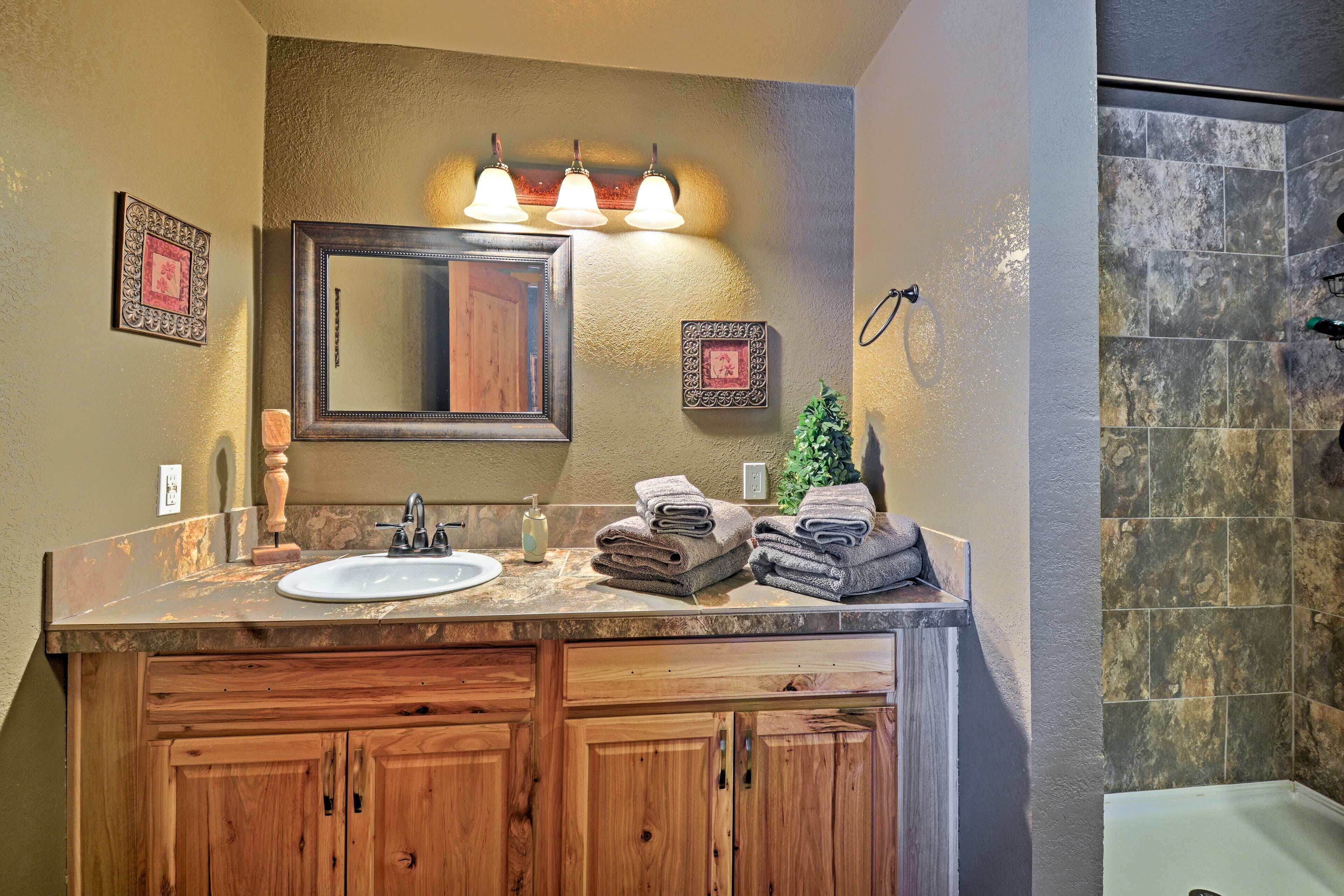 A bathroom with a wooden vanity, a sink, a mirror, and a shower area.