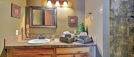 A bathroom with a wooden vanity, a sink, a mirror, and a shower area.