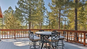 Une terrasse extérieure recouverte de neige, avec une table et des chaises, entourée de grands pins.