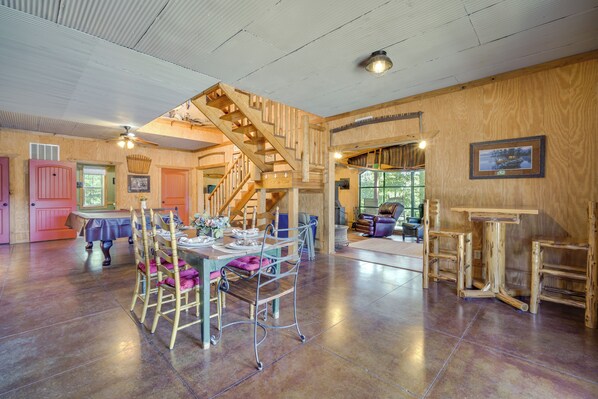 A spacious room with a wooden staircase, a dining area with a table and chairs, and a large window providing natural light.