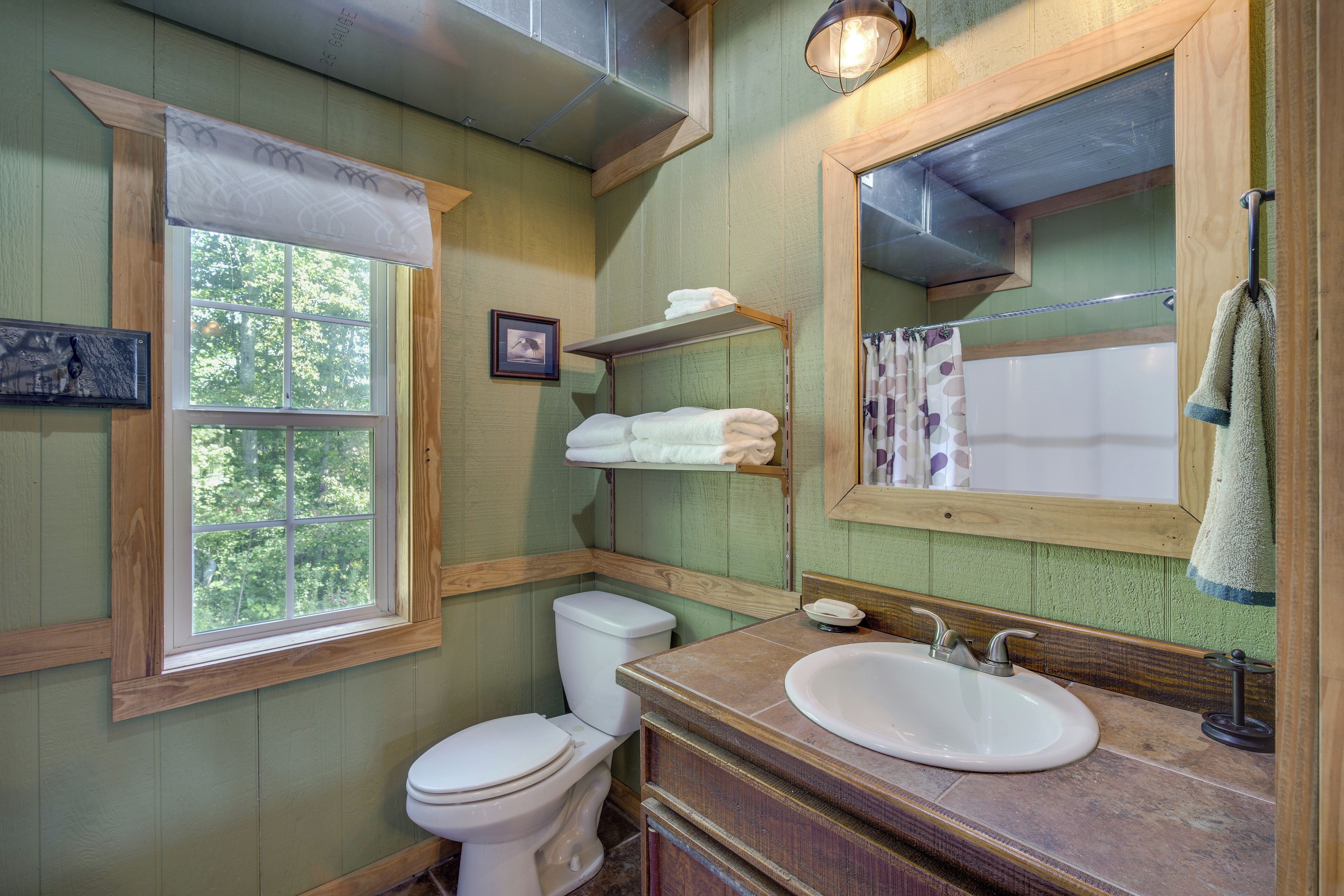 A bathroom with a wooden vanity, a sink, a toilet, and a window with a view of trees.