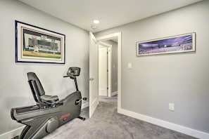 A home gym with a stationary bike, a framed baseball game photo, and a framed stadium photo on the walls.
