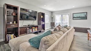 A living room with a large flat-screen TV, a sofa, a bookshelf, and a window with blinds. - Long Branch Getaway: Grill, 1 Block to Beach! (Long Branch)