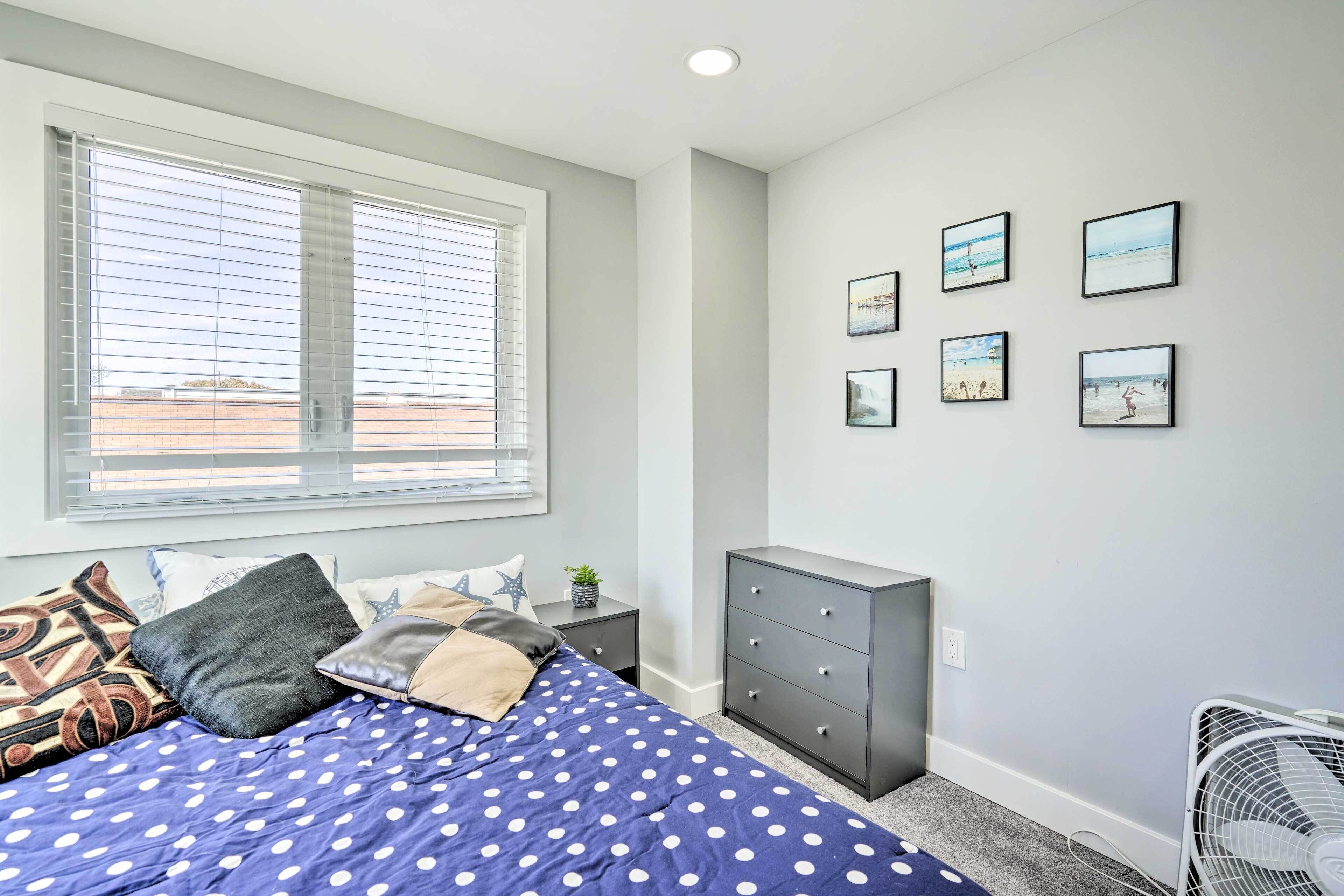 A bedroom with a bed, a dresser, a nightstand, a window with blinds, and wall art.