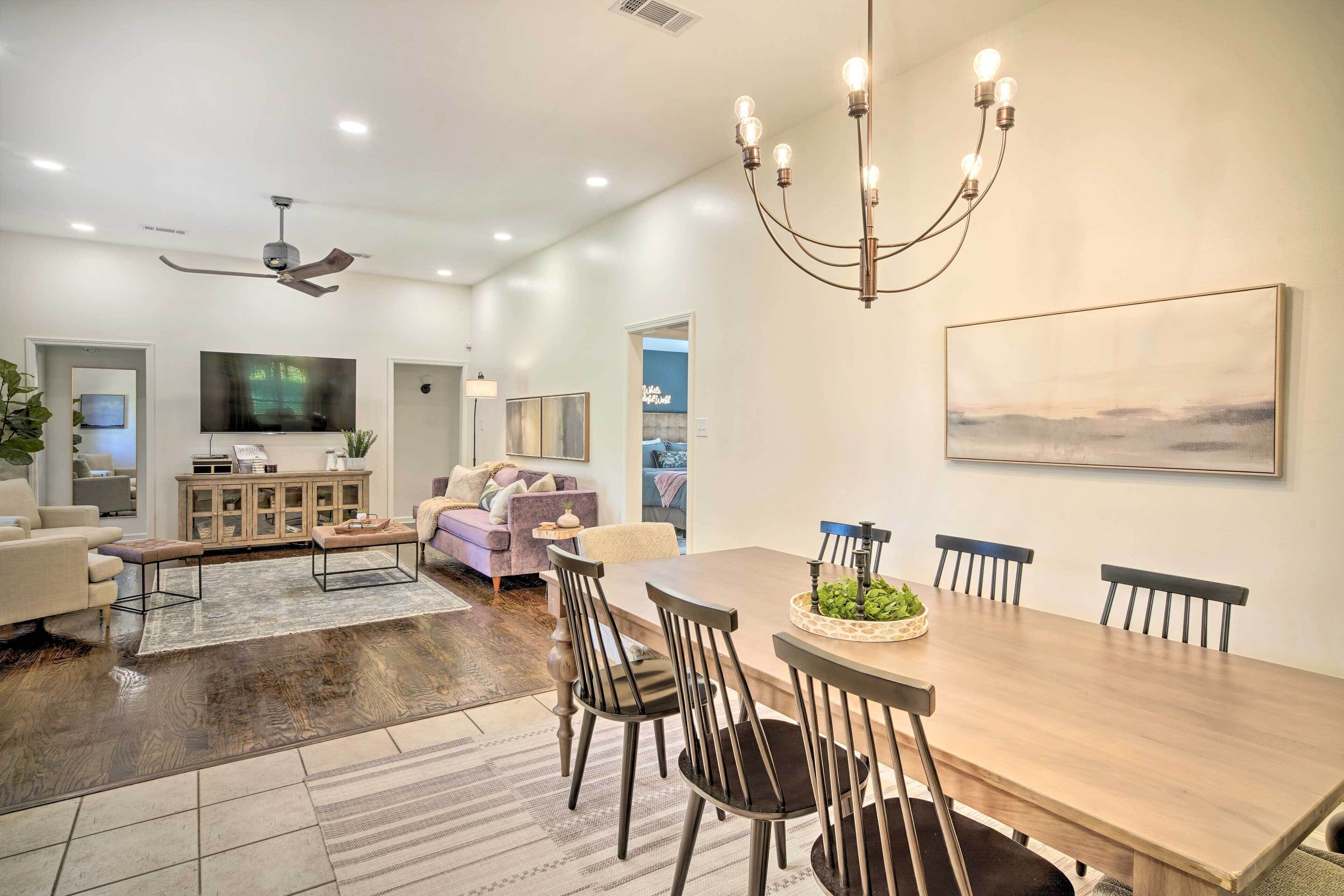 A spacious living room with a dining area, a ceiling fan, a chandelier, and a large painting on the wall.