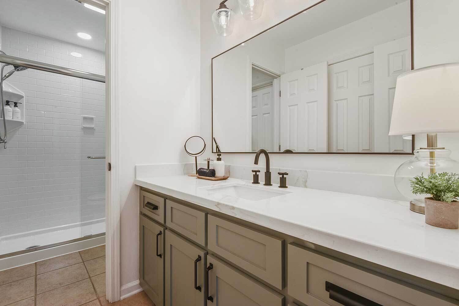 Un baño moderno con tocador blanco, un espejo grande y zona de ducha.