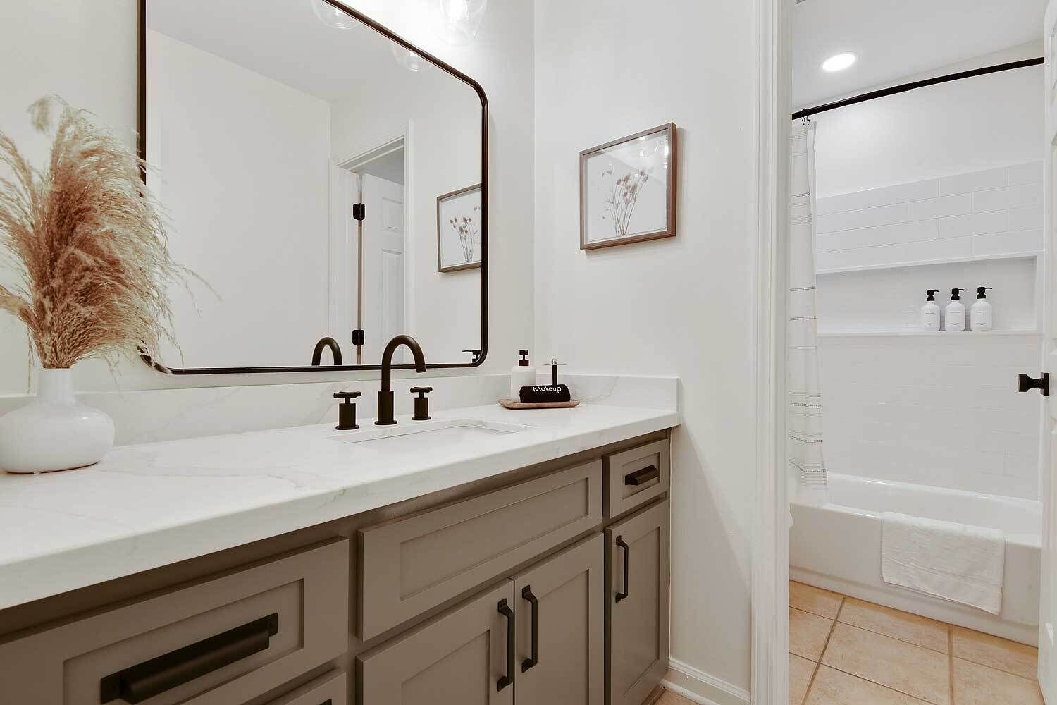A bathroom with a white vanity, a large mirror, a framed picture on the wall, and a shower area with a white curtain.