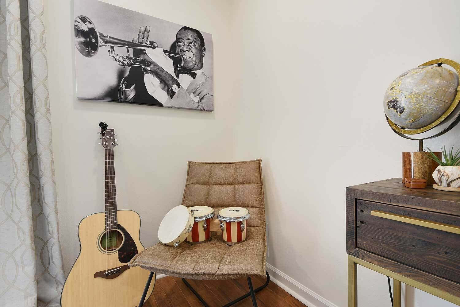 A room with a guitar, a chair with three drums, a globe on a stand, and a framed picture on the wall.