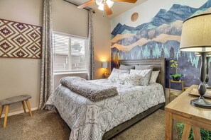 A bedroom with a bed, a bedside table, a lamp, a window with curtains, a wall mural, and a ceiling fan. - Private Patio + Gazebo: Show Low Hideaway! (Show Low)