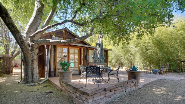 A wooden cabin with a patio, outdoor furniture, and a large tree providing shade.