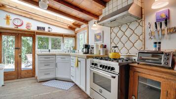 A kitchen with wooden beams, white cabinets, a stove, a toaster, and a window overlooking greenery.