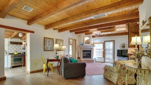 A spacious living room with wooden beams, a fireplace, and a dining area with yellow chairs.