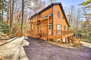 A wooden cabin with a balcony, a covered porch, and a driveway leading to the entrance.