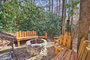 A wooden deck with benches and a stone fire pit surrounded by trees.
