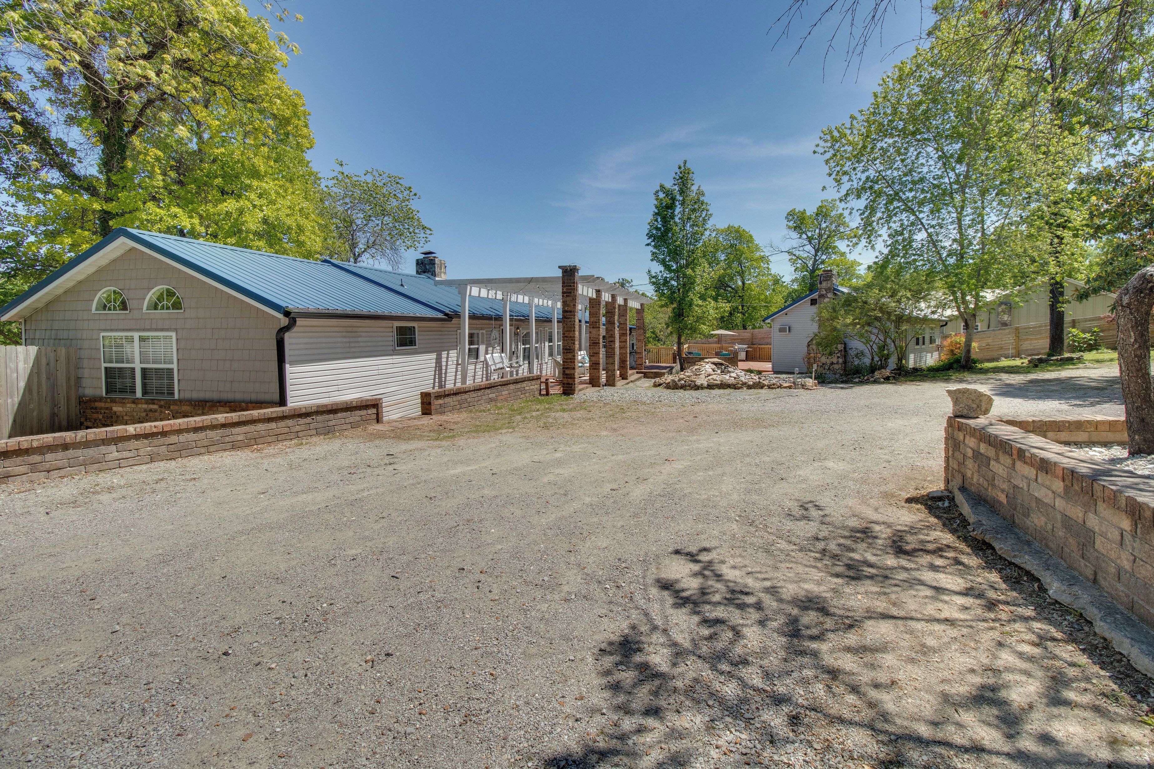 A residential area with a gravel driveway, a covered outdoor seating area, and a house with a blue roof.